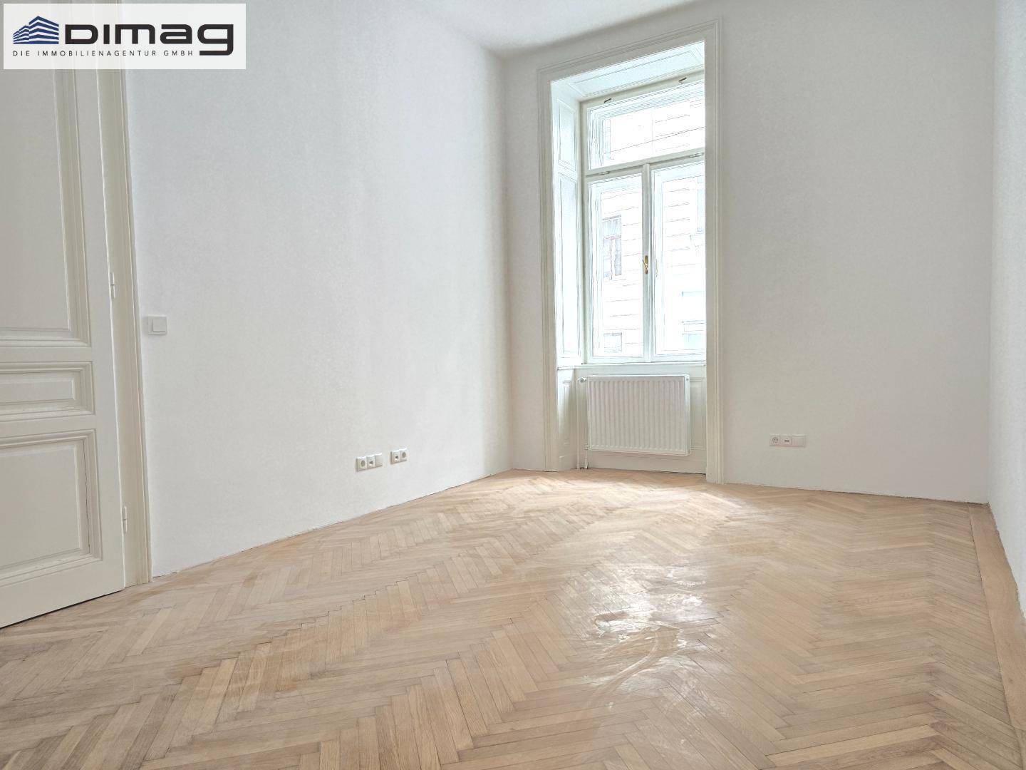 Geräumiger, heller Raum mit klassischem Fischgrätparkett und einem hohen Fenster, bereit zur individuellen Gestaltung.