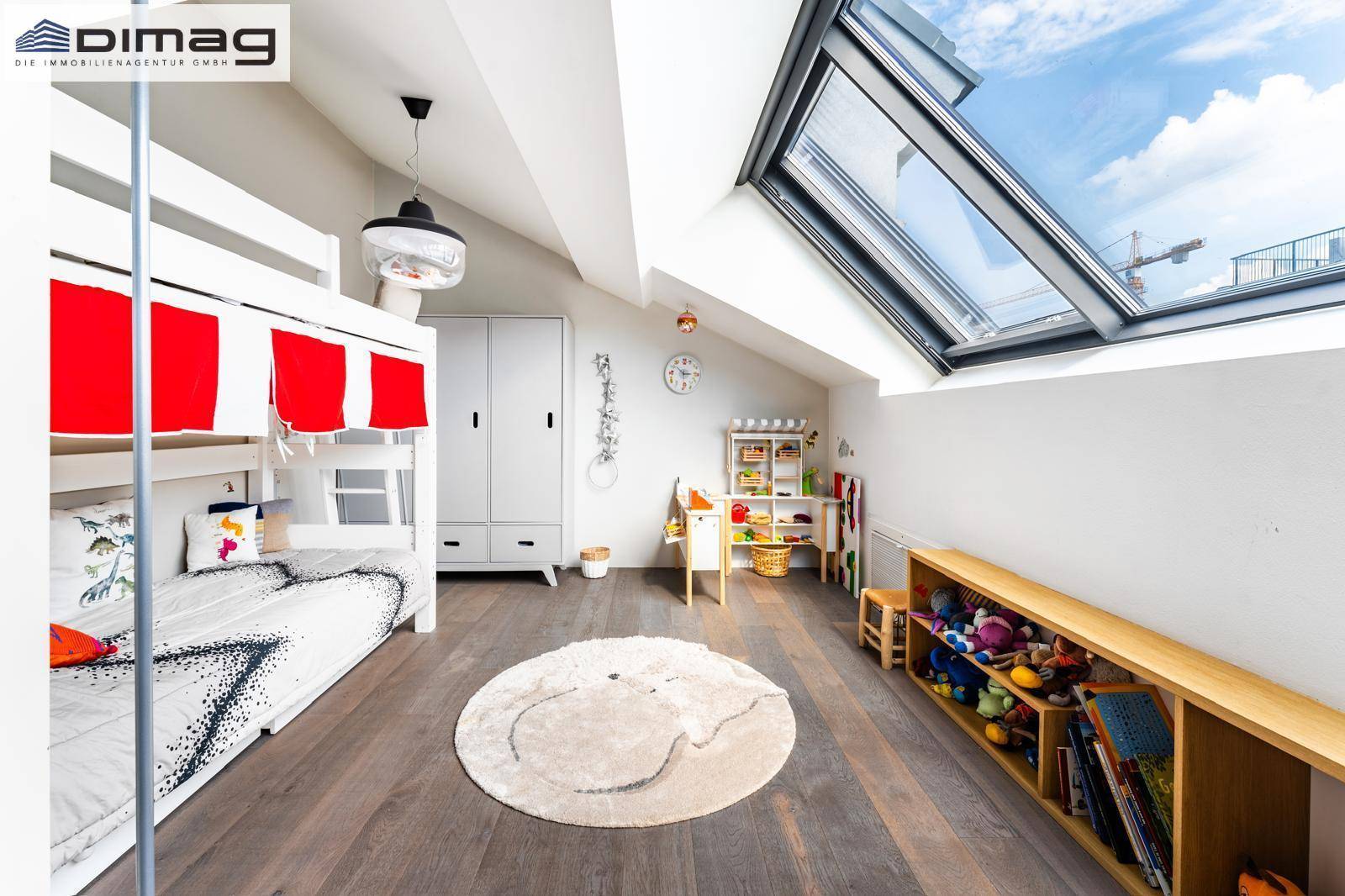Helles Kinderzimmer mit Etagenbett, großem Dachfenster und Spielzeugregalen unter der Dachschräge.