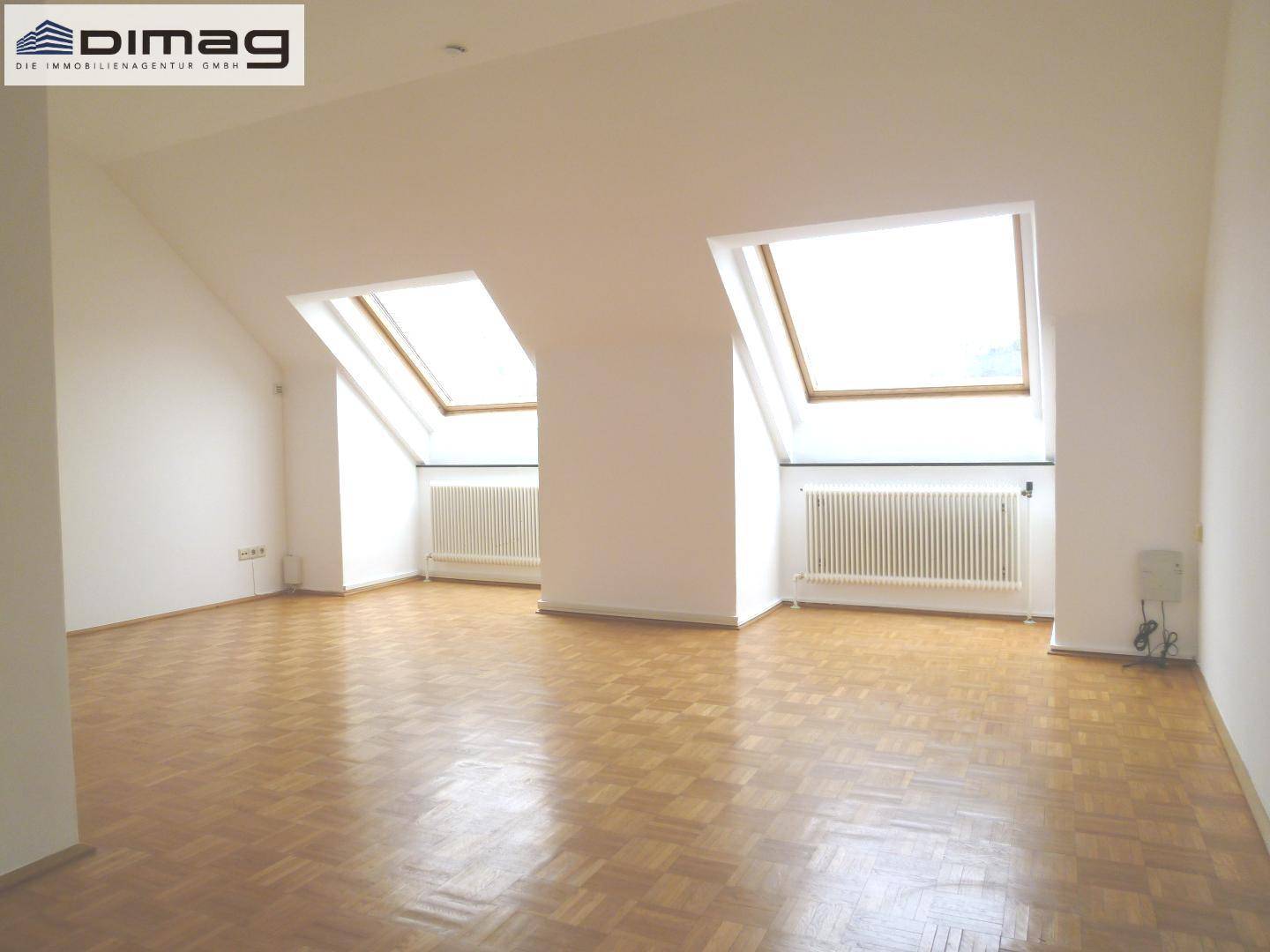 Geräumiges Zimmer im Dachgeschoss mit zwei Dachfenstern und Parkettboden.