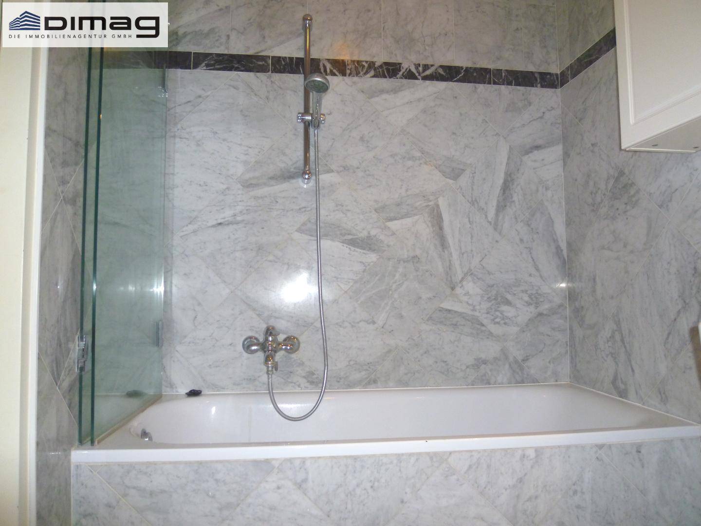 Badewanne mit Duschvorrichtung und Glasabtrennung in einem gefliesten Badezimmer.