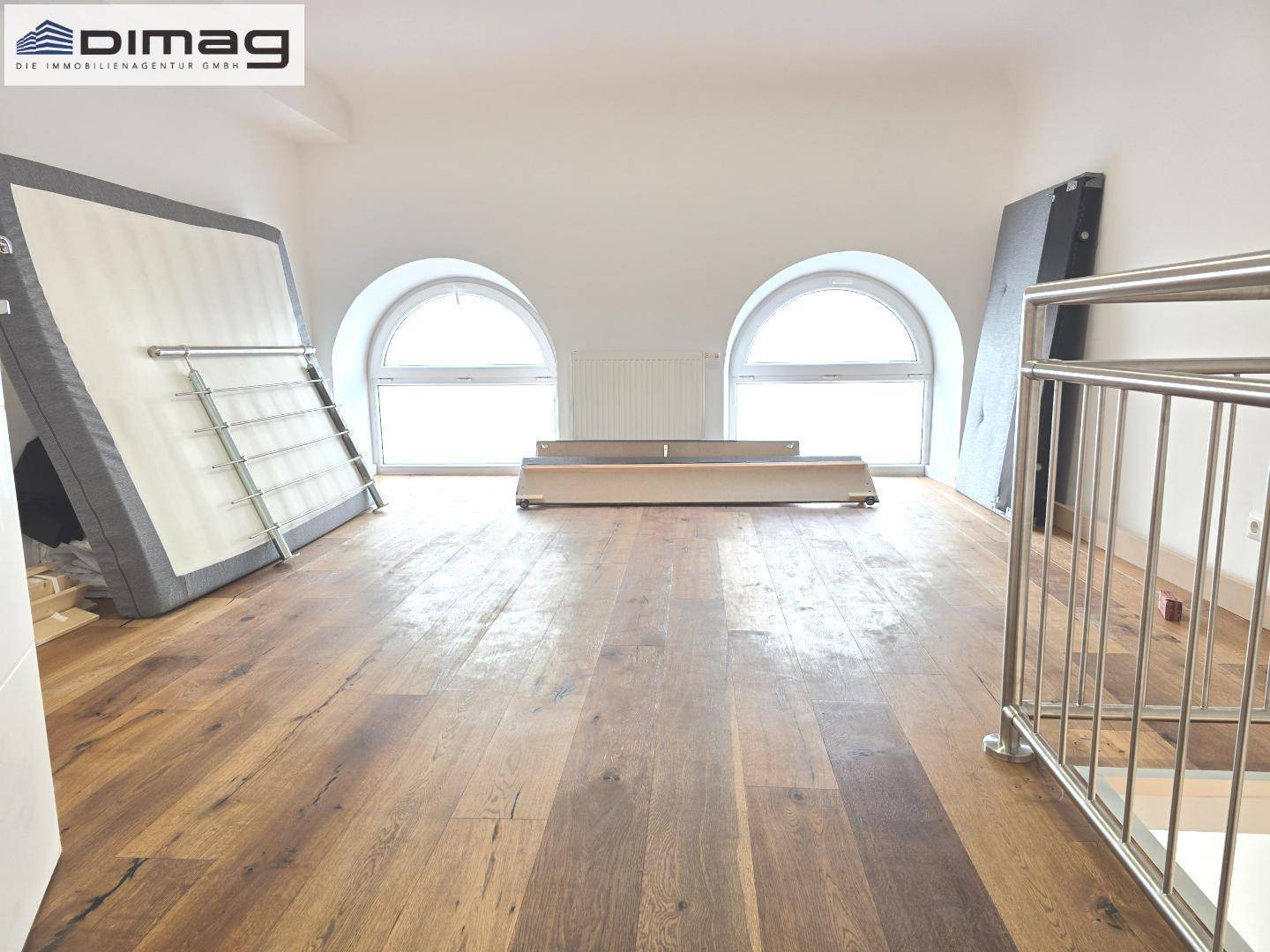 Helles Schlafzimmer im Dachgeschoss mit Holzboden, zwei Rundbogenfenstern und viel natürlichem Licht.