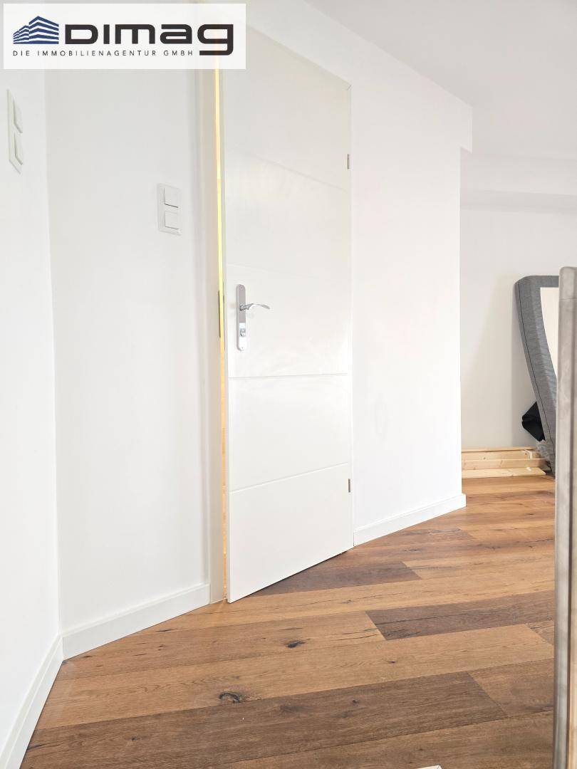 Heller Flur mit weißer Tür und elegantem Holzboden, der zu weiteren Räumen führt.