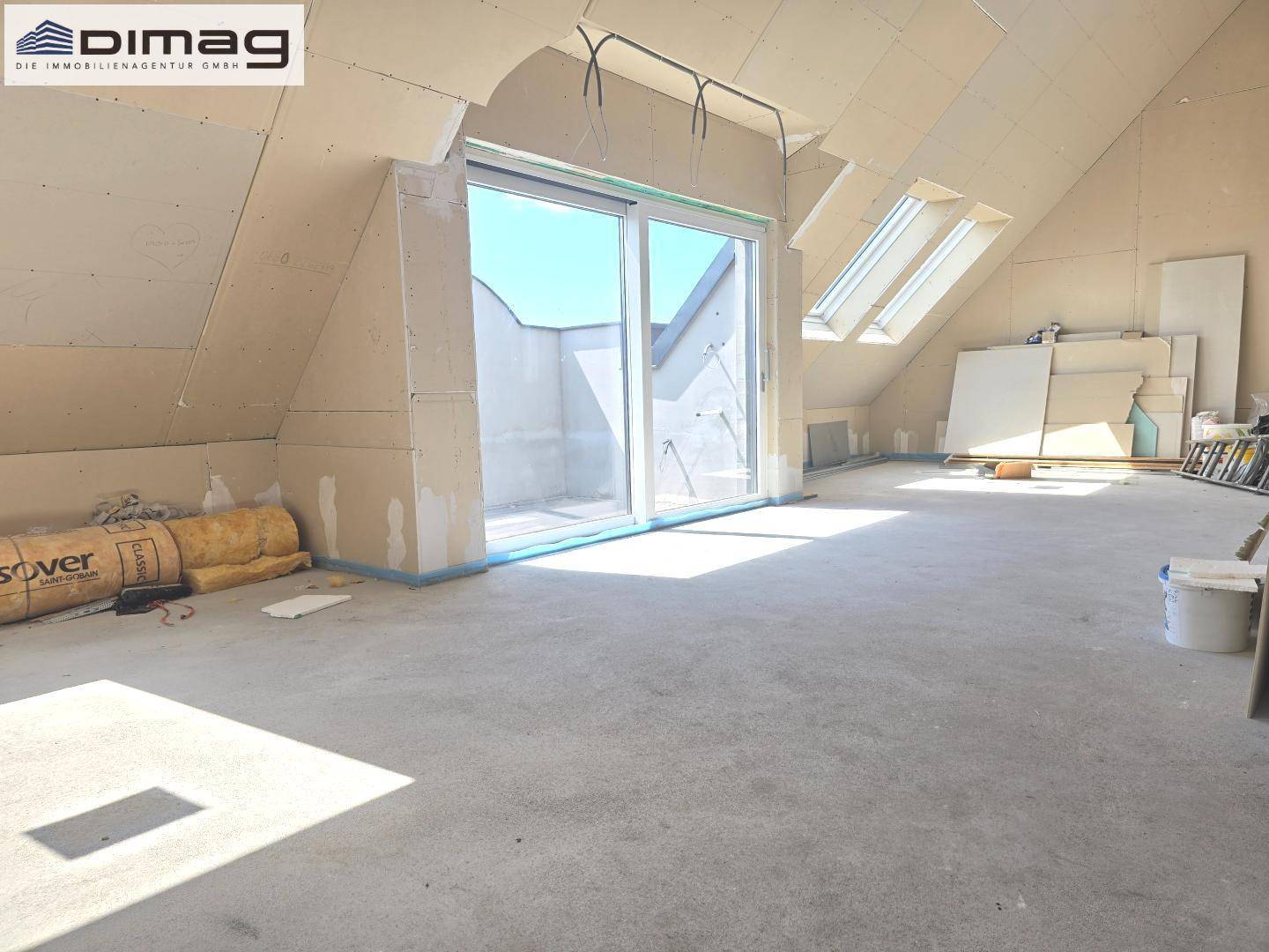 Heller Rohbau im Dachgeschoss mit Dachfenstern und Zugang zur Terrasse.