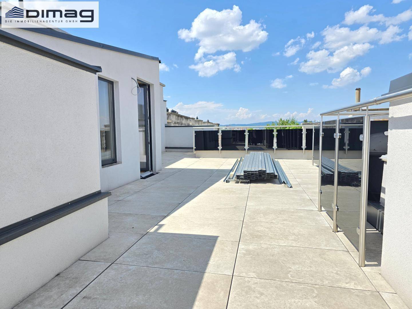 Weitläufige Dachterrasse im Rohbau mit Zugang zum Innenbereich und Stadtblick.
