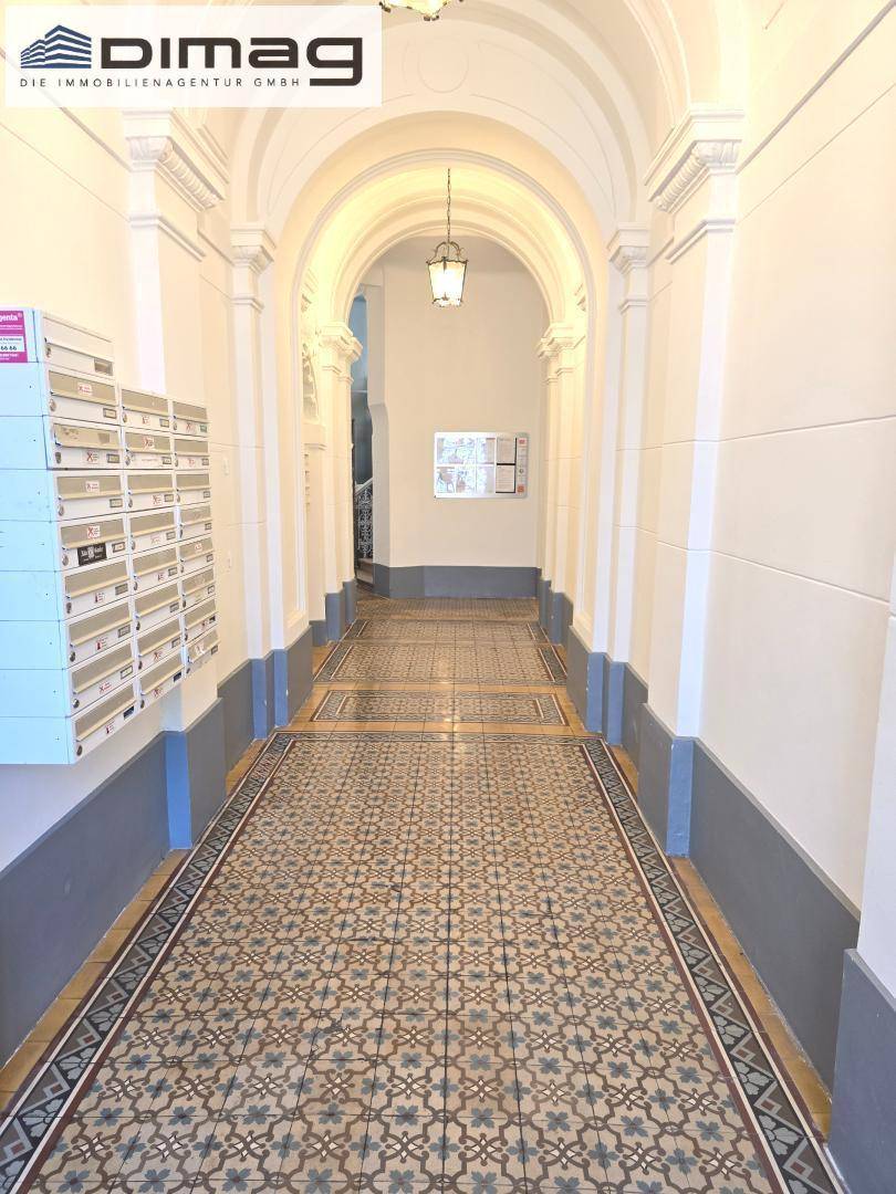 Historischer Eingangsbereich mit hohen Gewölbedecken, dekorativen Fliesen und Briefkästen.