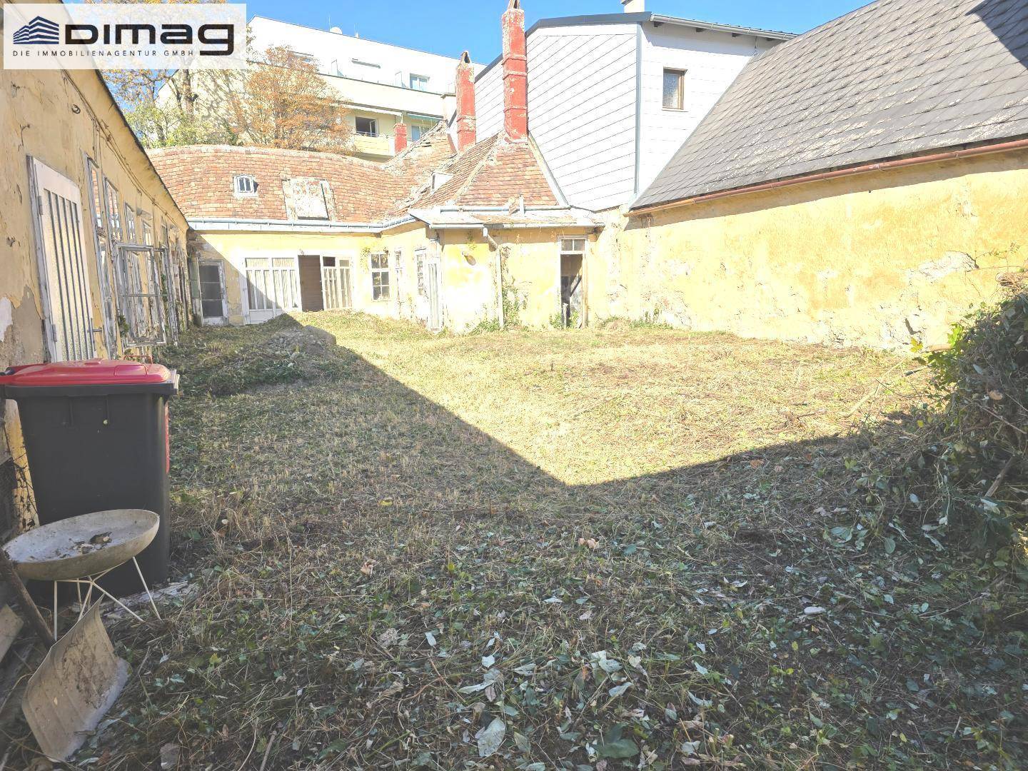 Blick auf den verwilderten Innenhof mit alten Gebäuden und viel Unkraut, das aufgeräumt werden muss.