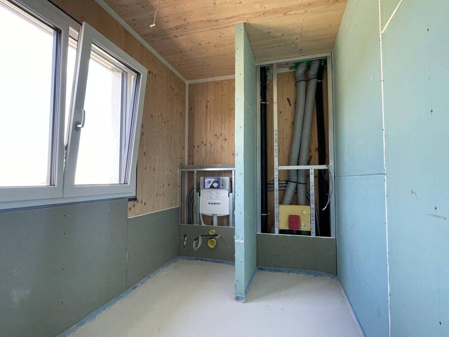 Unfertiges Badezimmer mit Holzverkleidung, Fenster und sichtbaren Installationen, bereit für den Ausbau.