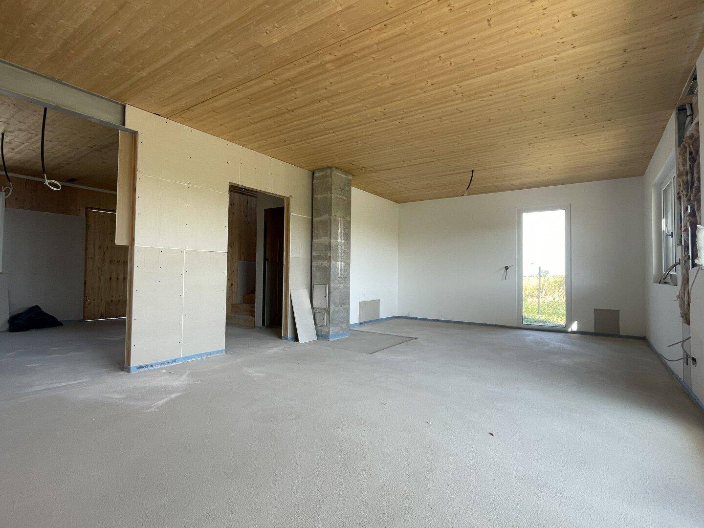 Geräumiger, unfertiger Innenraum mit Holzdecke und Blick ins Grüne, bereit für den Ausbau.