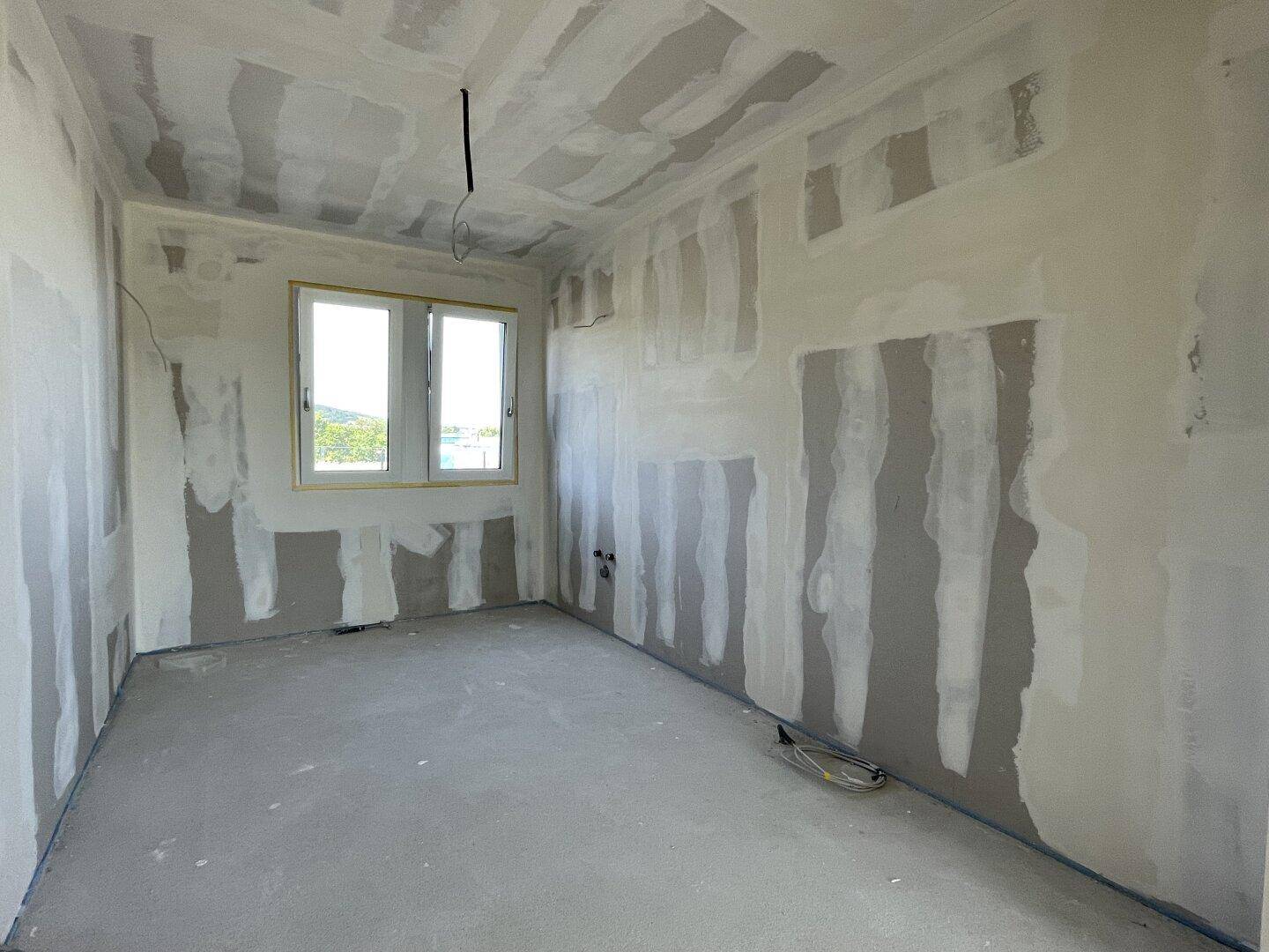 Helles, unfertiges Schlafzimmer mit Fenster und Blick ins Grüne, bereit für den Innenausbau.