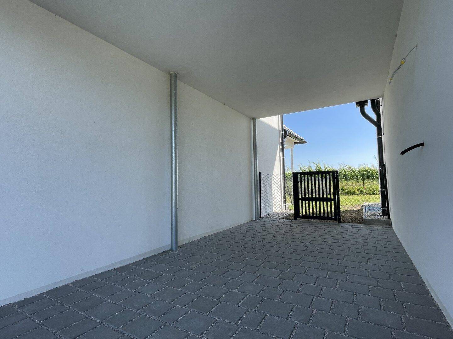 Überdachter Stellplatz mit gepflastertem Boden und Zugang zu einem angrenzenden Feld.
