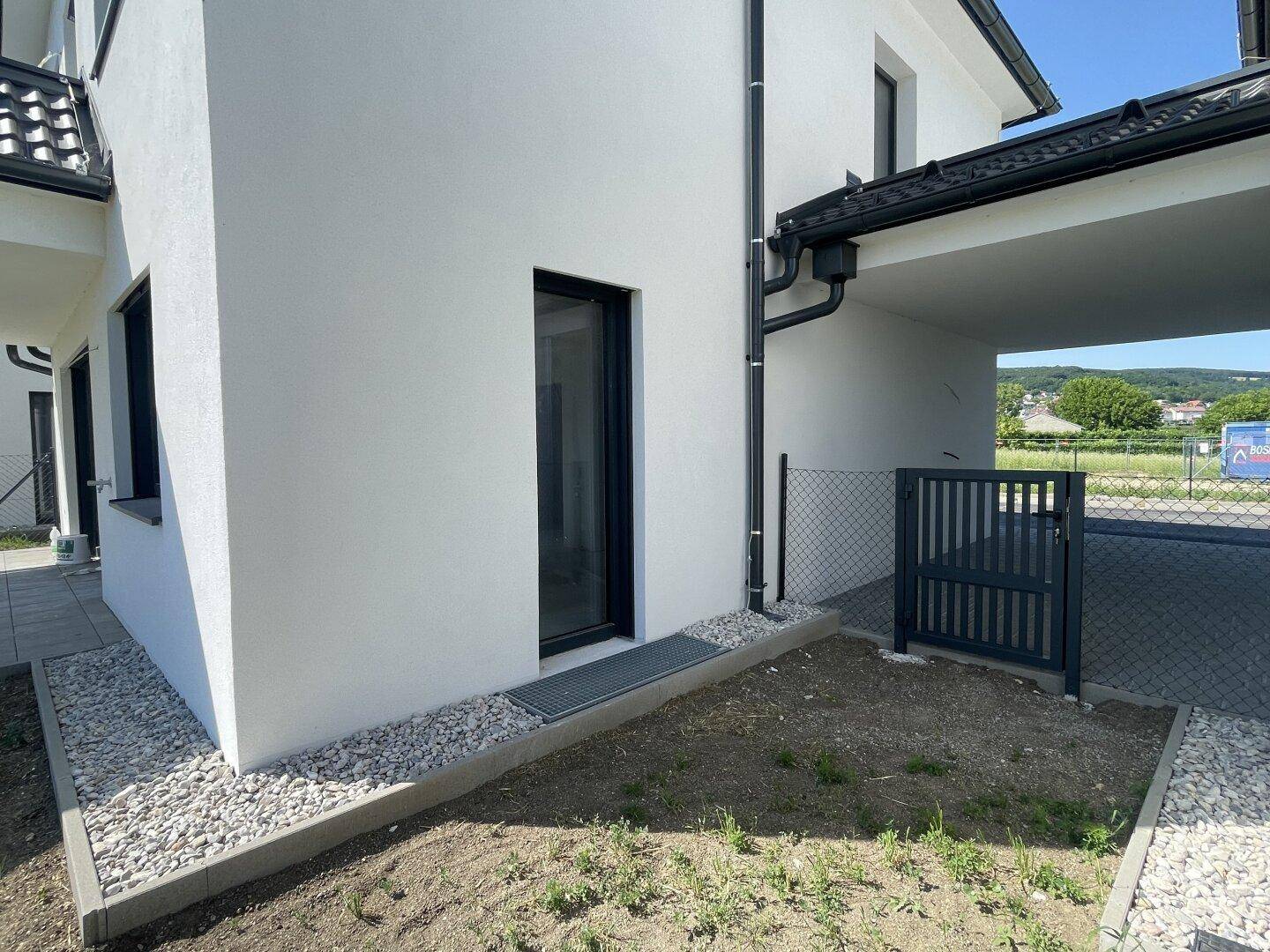 Moderne weiße Fassade eines Neubaus mit schwarzen Akzenten und einem Carport.