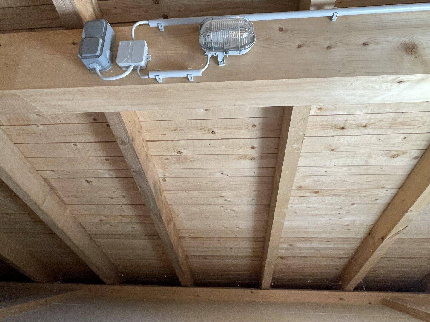 Detailansicht der Holzdecke im Dachboden mit sichtbaren Brettern und einfacher elektrischer Installation.
