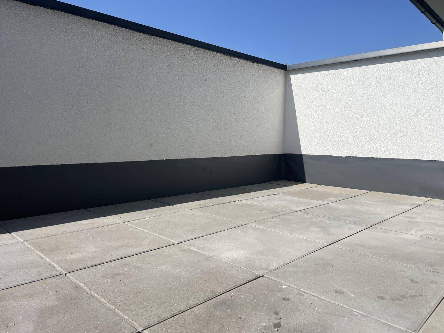Große, gepflasterte Terrasse mit hohen weißen Wänden unter blauem Himmel, ideal für Entspannung.