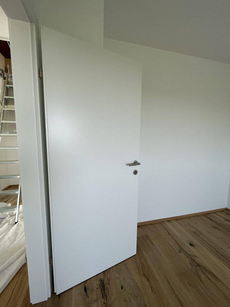 Heller Raum mit einer modernen weißen Tür und neu verlegtem Holzboden, bereit zur Einrichtung.