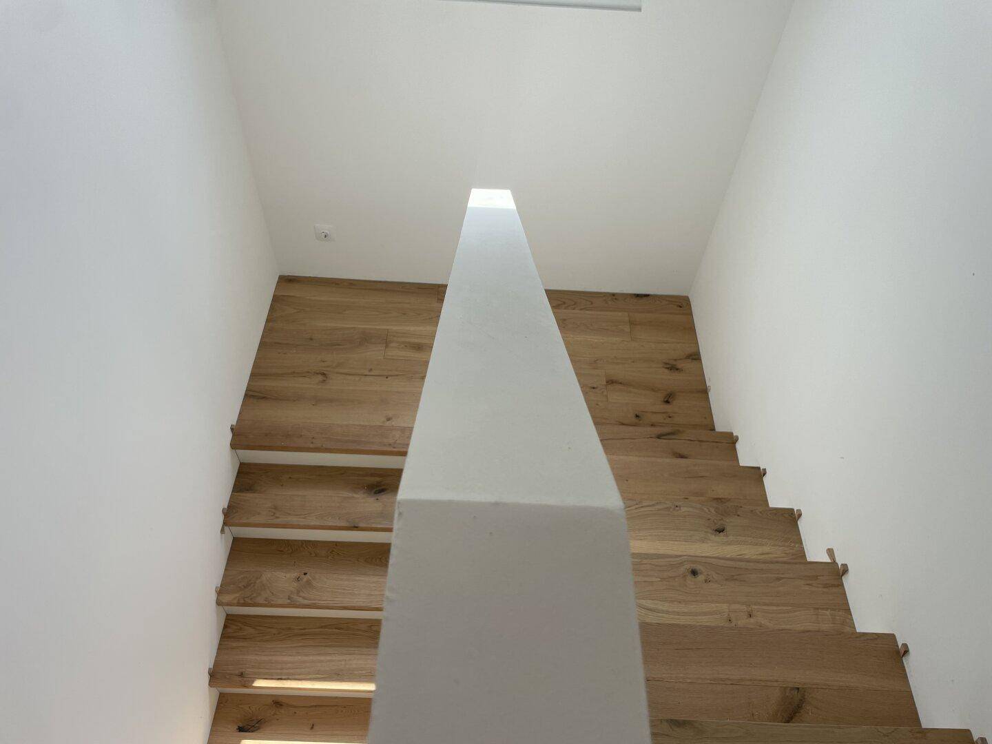 Moderne Holztreppe mit hellem Geländer und weiß gestrichenen Wänden, die nach oben führt.