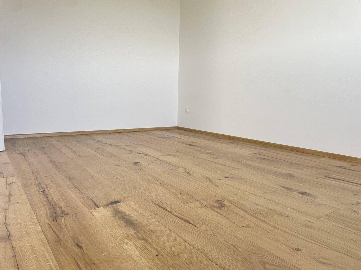 Leerer Raum mit neuem Holzboden und weißen Wänden, bietet vielseitige Gestaltungsmöglichkeiten.