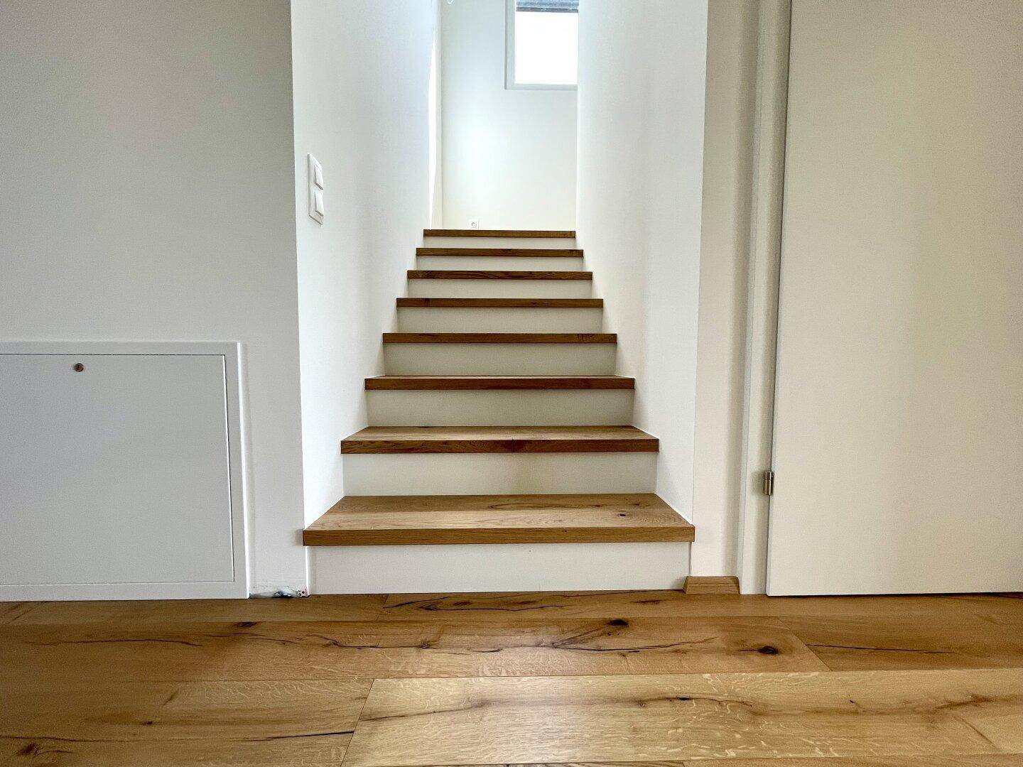 Moderne Holztreppe im Flur mit hellem Dielenboden und weiß gestrichenen Wänden.