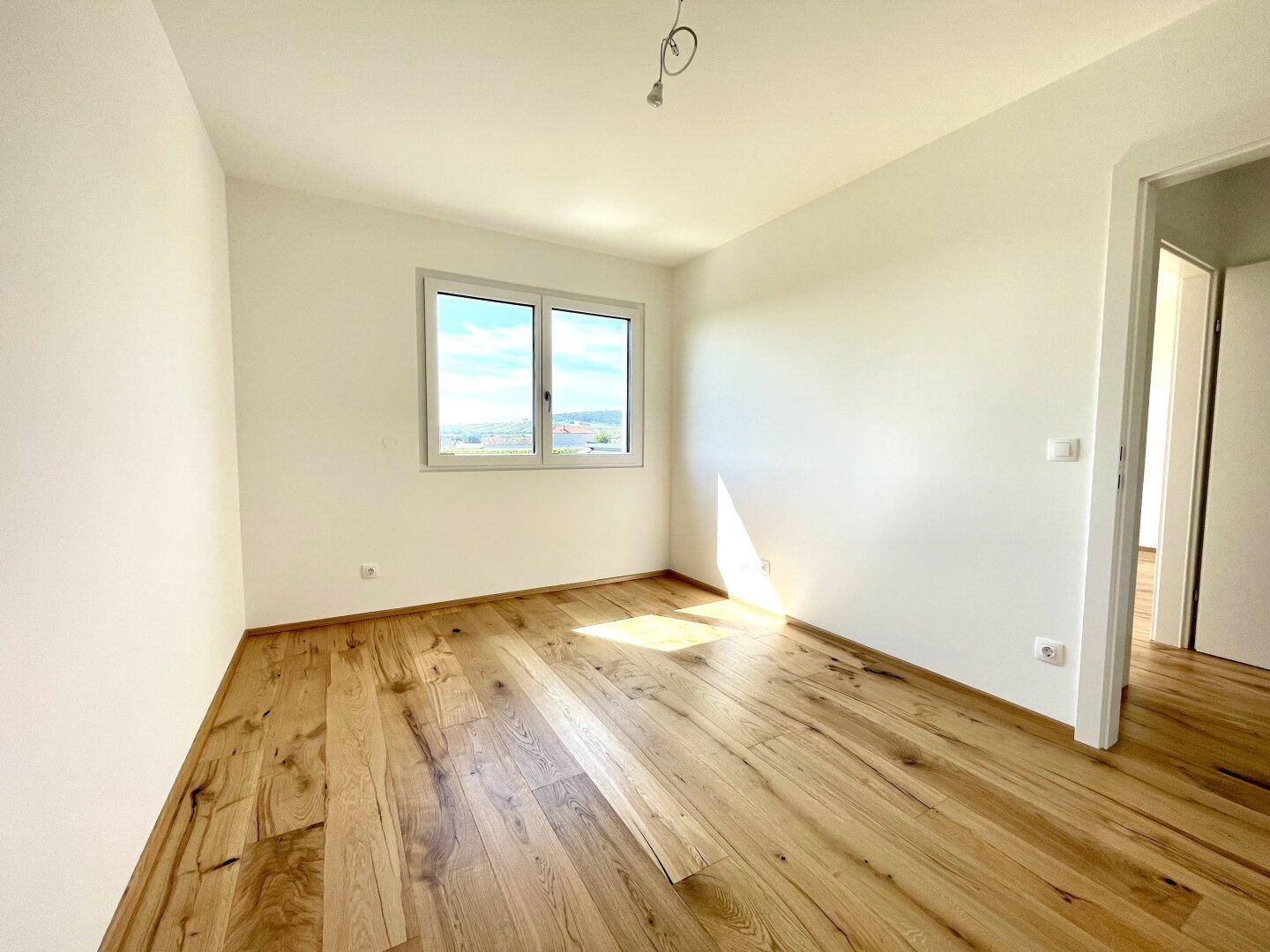 Helles Schlafzimmer mit Holzboden, großem Fenster und weitem Blick in die Landschaft.