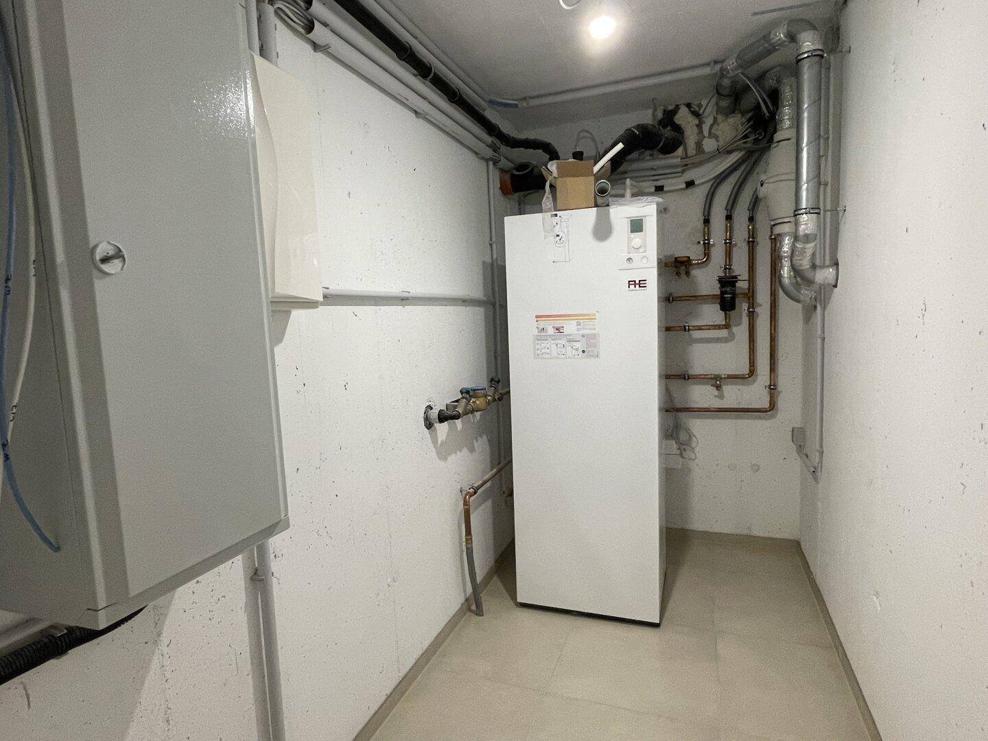 Technikraum mit moderner Wärmepumpe, Rohrleitungen und elektrischen Installationen.
