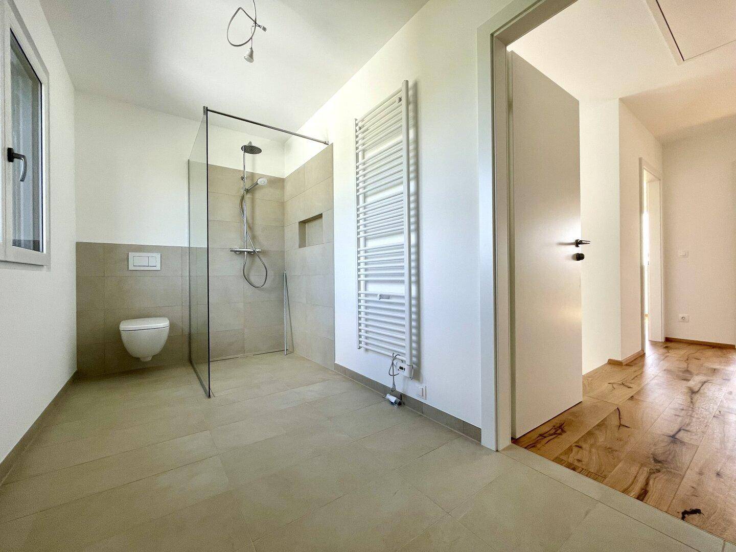 Geräumiges Badezimmer mit moderner Dusche und Zugang vom Flur mit Holzdielenboden.