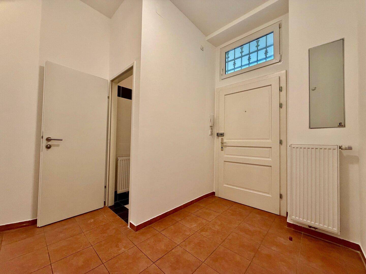 Heller Eingangsbereich mit Terrakotta-Fliesenboden, weiß gestrichenen Wänden und einer Eingangstür mit Oberlicht.