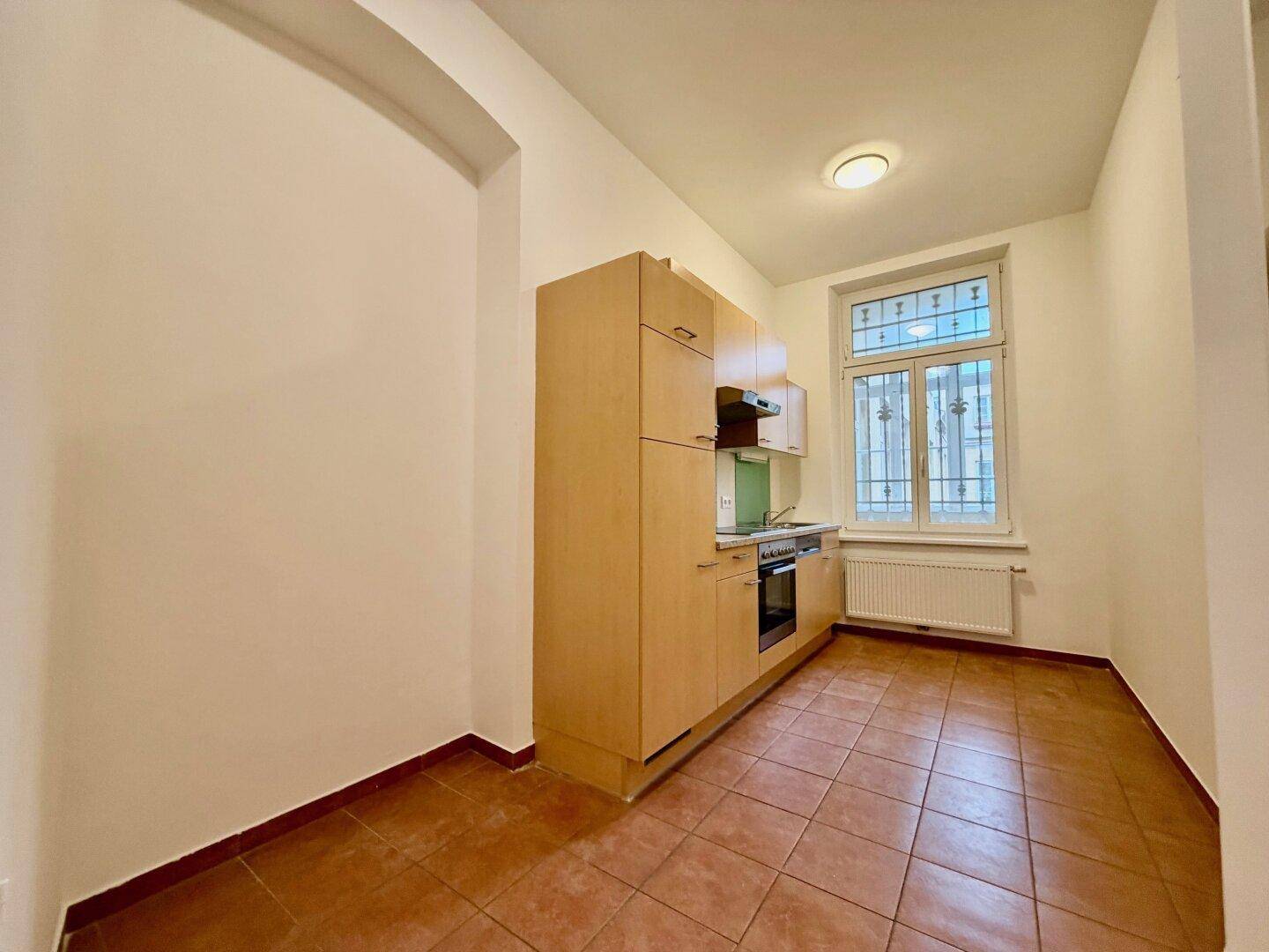 Kompakte Küche mit Holzschränken, Granitarbeitsplatte und einem Fenster, das Tageslicht in den Raum bringt.