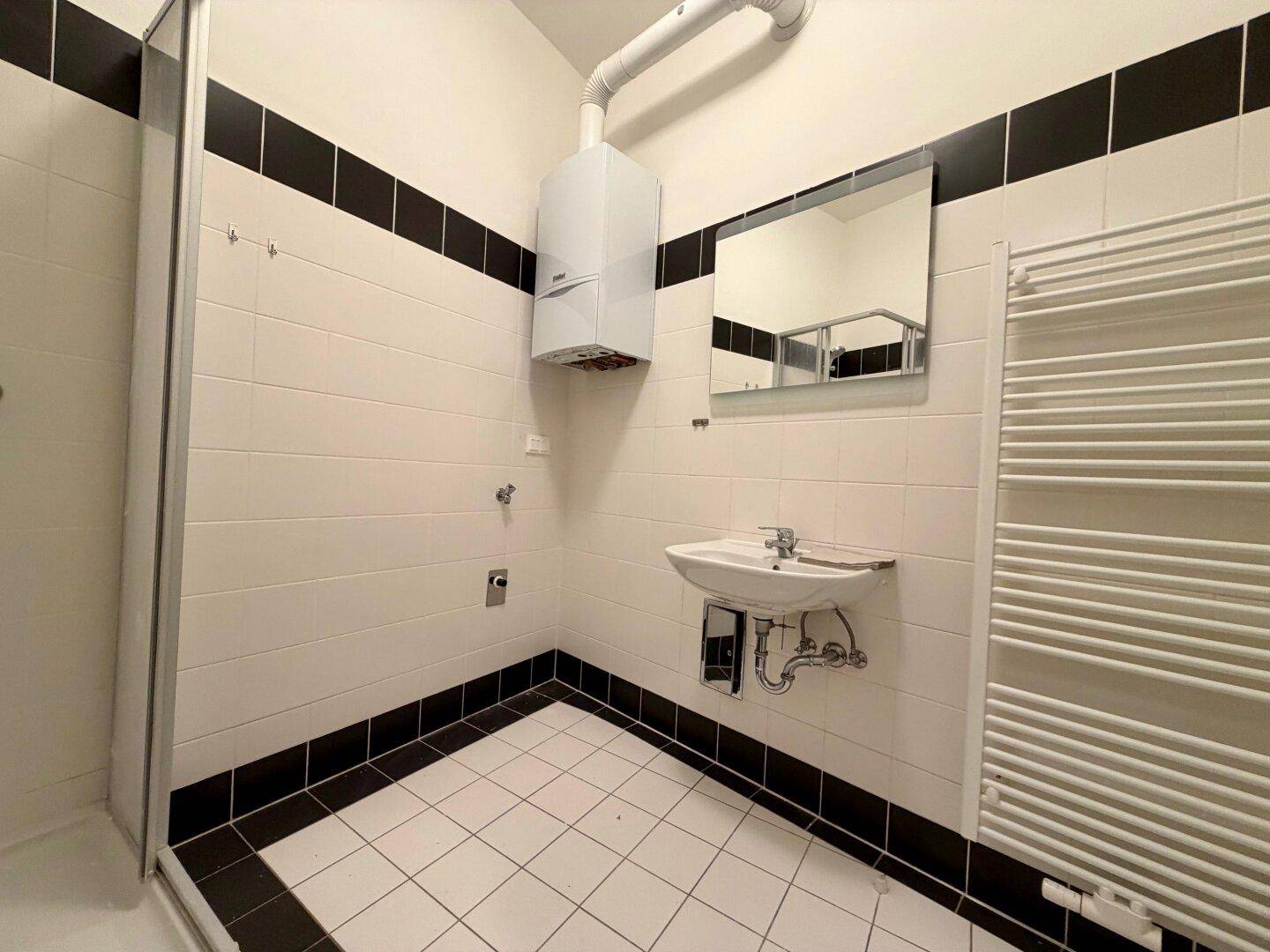 Badezimmer mit Duschkabine, Waschbecken, Spiegel und Handtuchheizkörper, in klarem Schwarz-Weiß-Design.