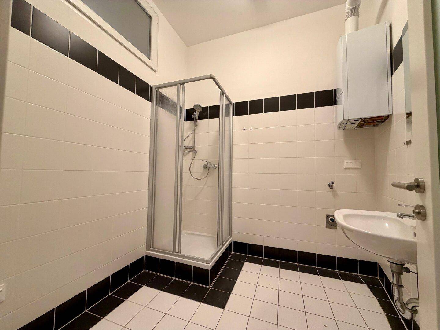 Modern gefliestes Badezimmer mit Duschkabine, Waschbecken und Gastherme, in Schwarz-Weiß-Kontrast gehalten.