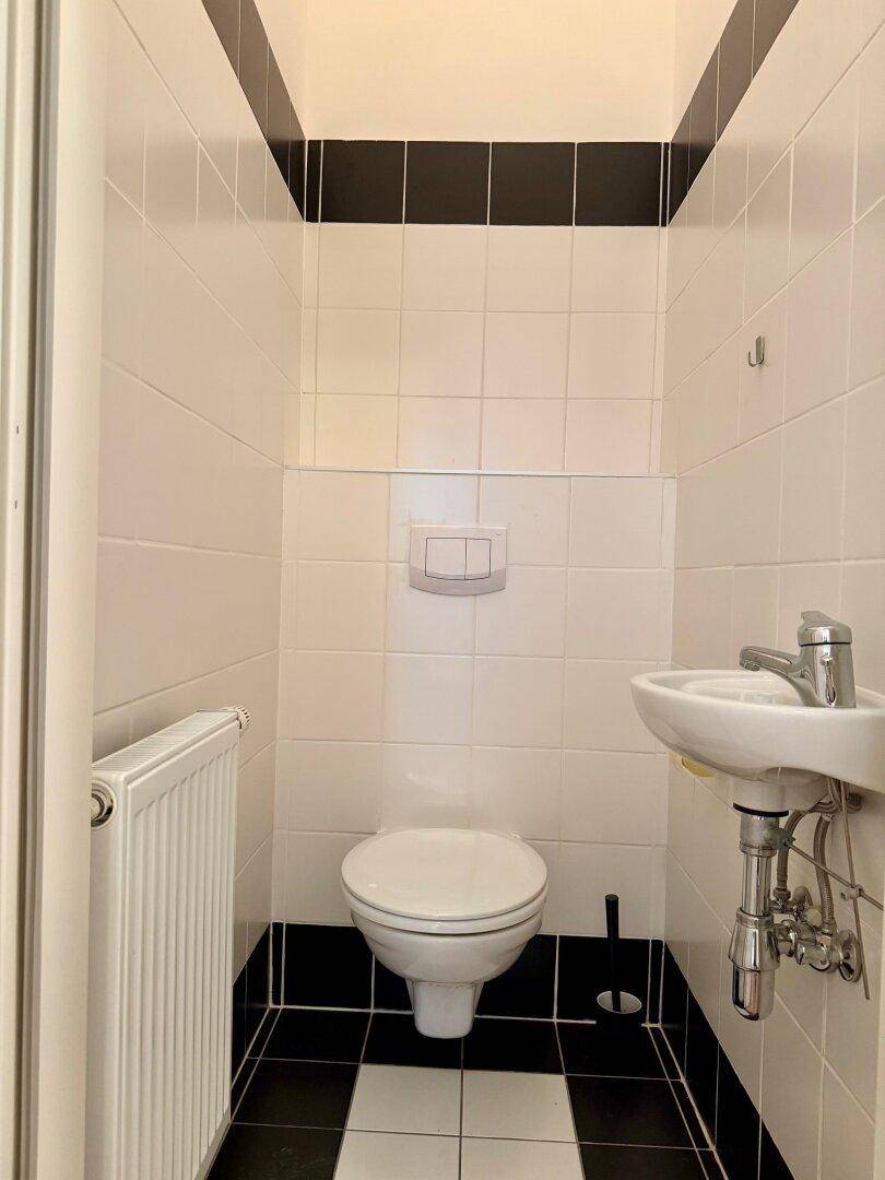 Separate Gästetoilette mit Wand-WC, kleinem Waschbecken und Heizkörper, in Schwarz-Weiß-Fliesenoptik.