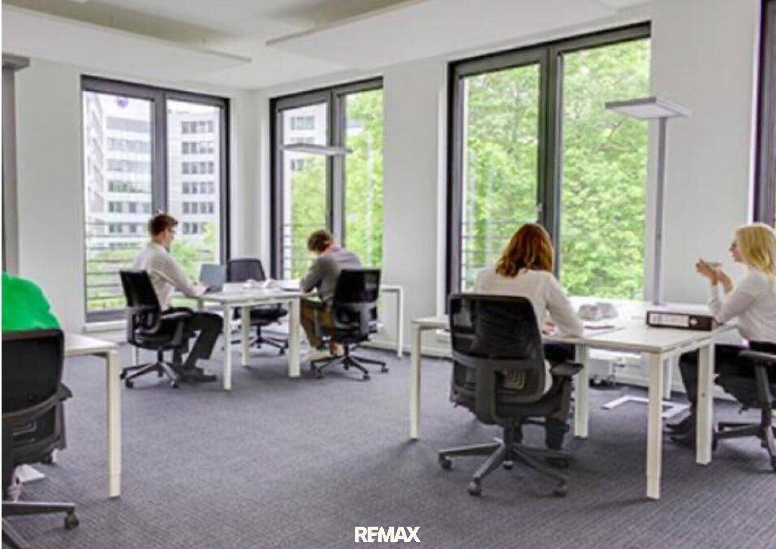 Helles und modernes Büro mit großen Fenstern, Blick ins Grüne und mehreren Arbeitsplätzen.