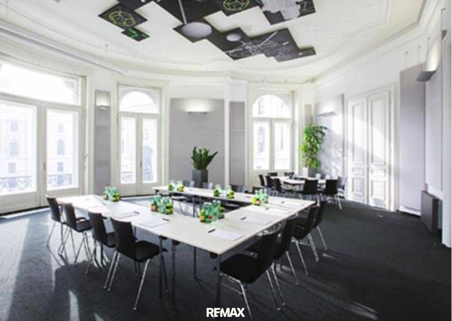 Eleganter Konferenzraum mit hohen Fenstern, Stuckdecken und einem großen U-förmigen Tisch für Besprechungen.
