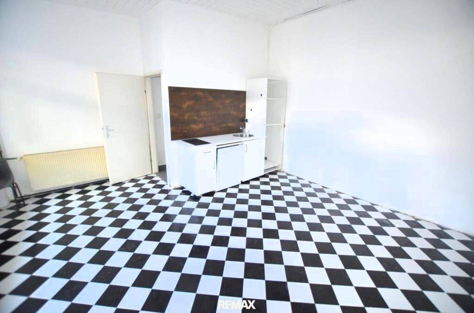 Heller Raum mit schwarz-weißem Fliesenboden und einer kleinen Küchenzeile an der Wand.