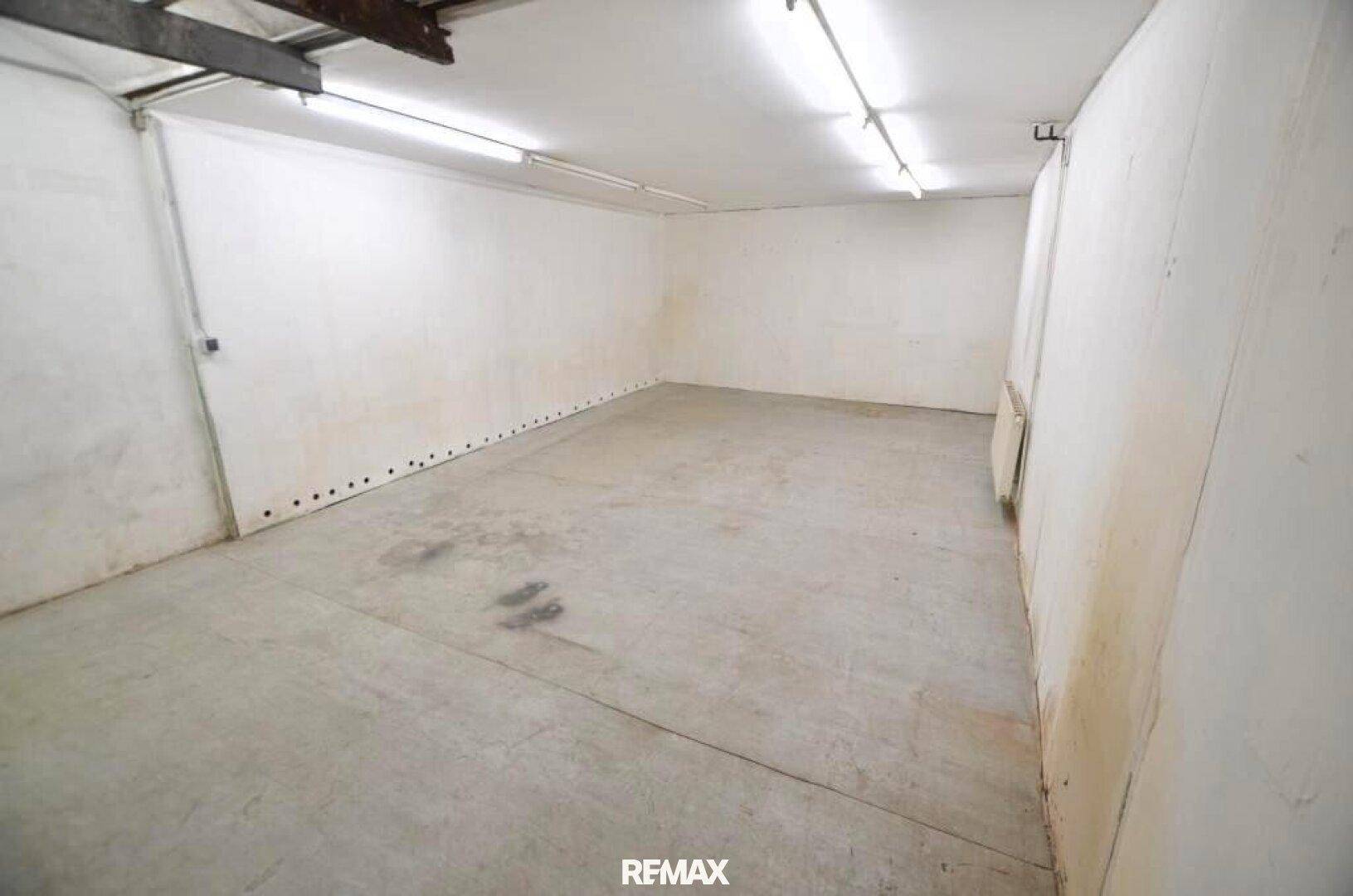 Leerer, funktionaler Raum mit Betonboden, sichtbaren Deckenbalken und Leuchtstoffröhren an der Decke.
