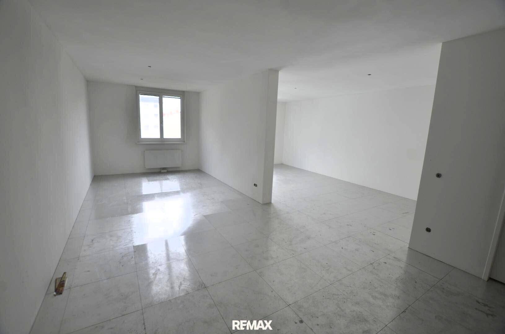 Heller, leerer Innenraum mit großen Fliesen und einem Fenster, das viel Tageslicht hereinlässt.