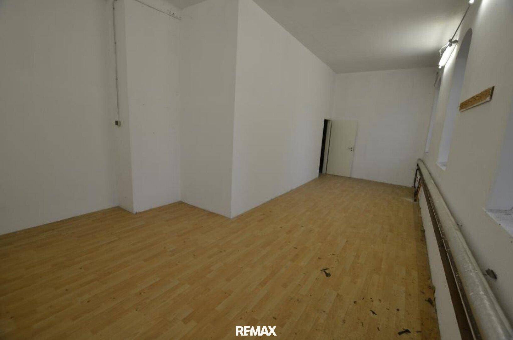 Geräumiger leerer Raum mit Holzboden und weißen Wänden, mit einer Tür und einem Fenster auf der rechten Seite.