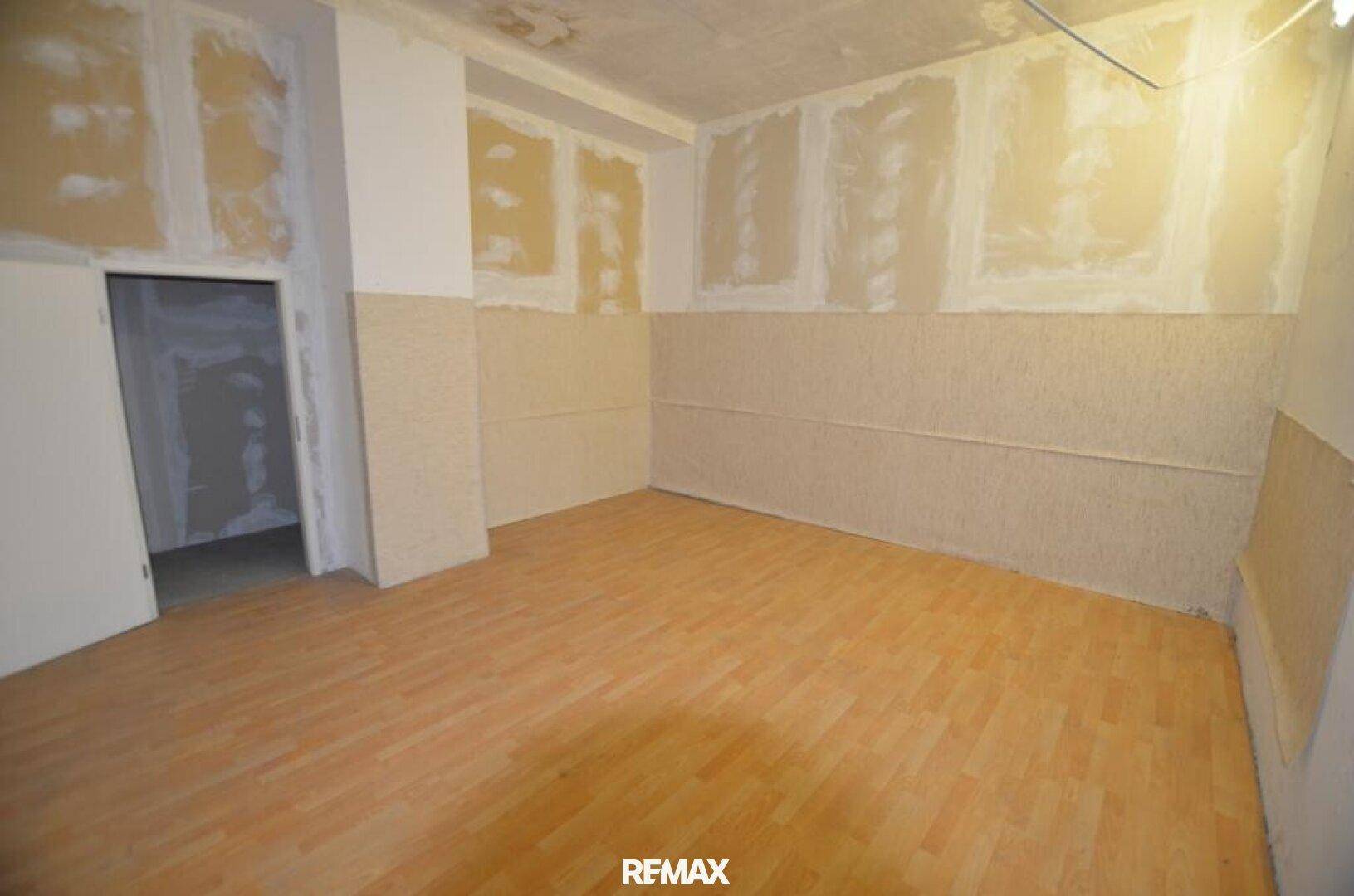 Ein Raum in Renovierung mit hellem Laminatboden und teilweise vorbereiteten Wänden, bereit für den Ausbau.
