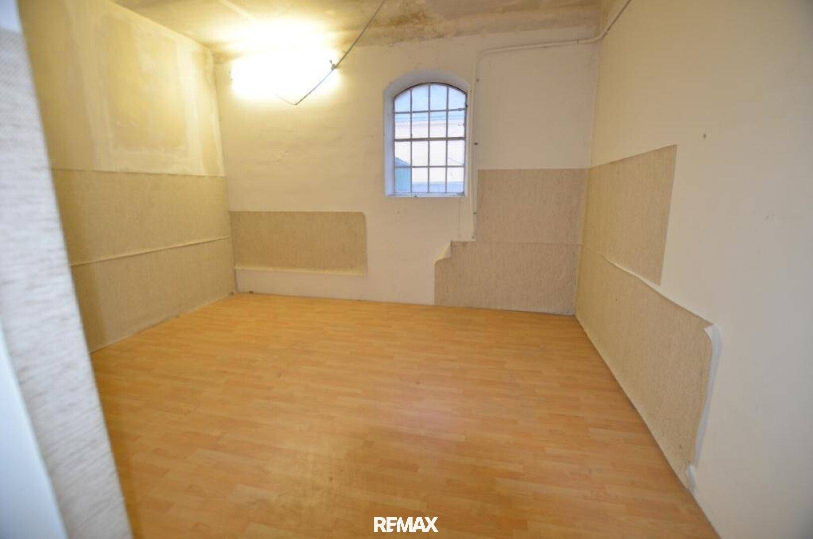 Leerer Raum mit Holzboden und einem Bogenfenster, teilweise unverputzte Wände, ideal für Lagerung.