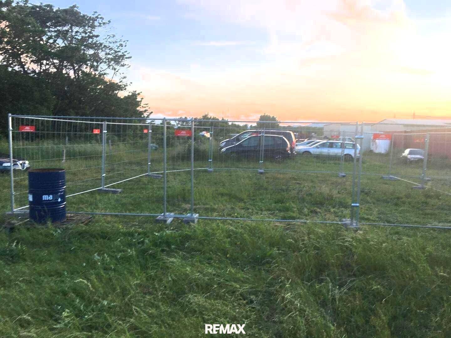 Grundstück mit temporärem Bauzaun und parkenden Autos im Hintergrund bei Sonnenuntergang.