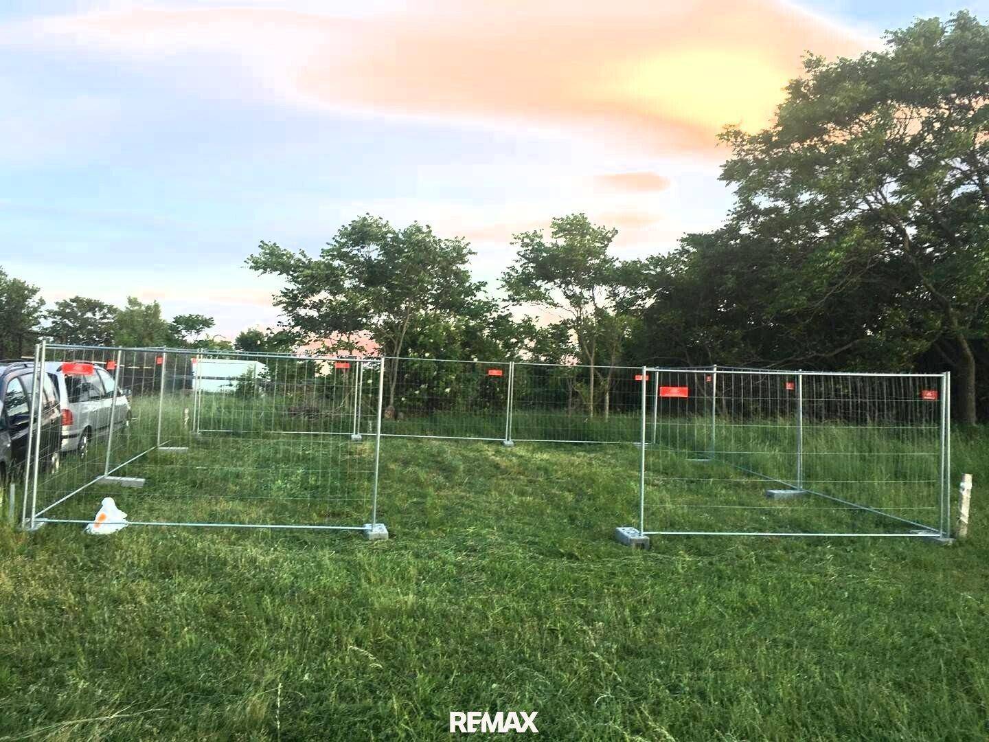 Weitläufiges grasbewachsenes Grundstück mit temporären Zäunen und einer Reihe von Bäumen im Hintergrund unter einem Abendhimmel.