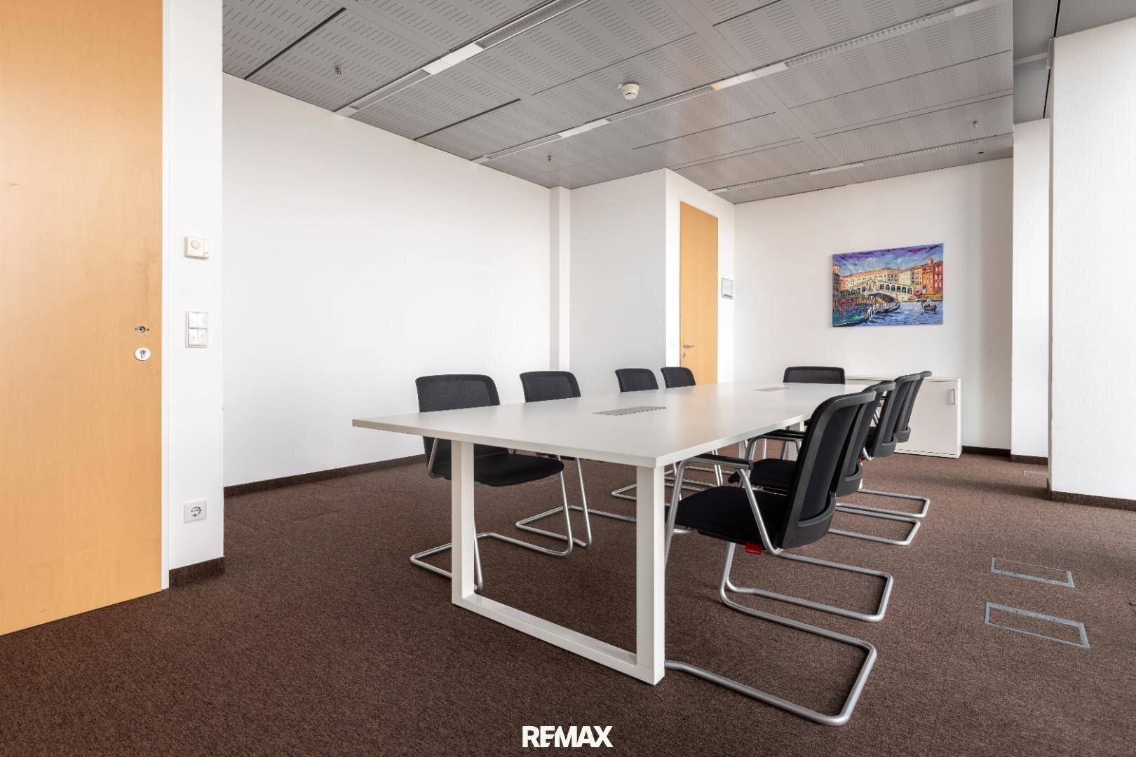 Geräumiger Konferenzraum mit großem Tisch, bequemen Stühlen und moderner Deckenbeleuchtung für produktive Meetings.