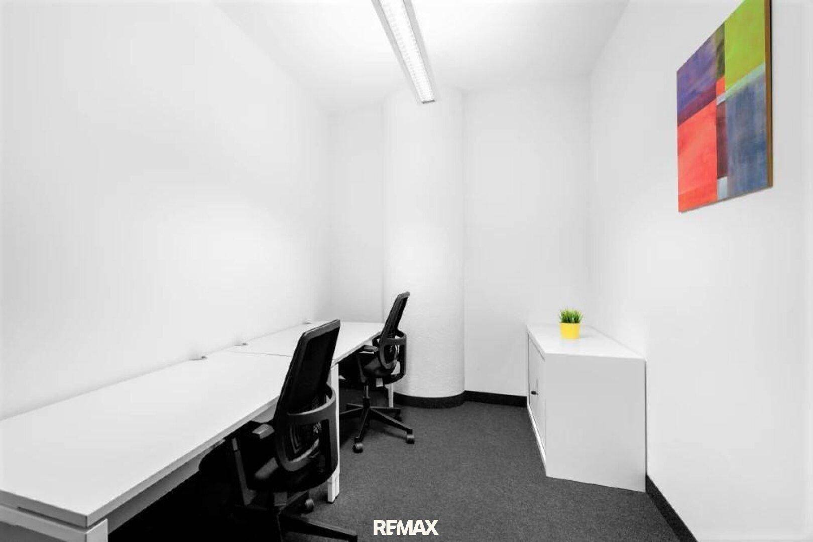 Helles, minimalistisches Büro mit zwei Arbeitsplätzen, Teppichboden und moderner Kunst an der Wand.