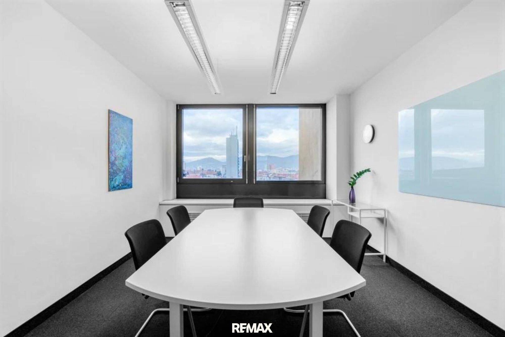 Geräumiger Konferenzraum mit großem Besprechungstisch, Teppichboden und weitem Stadtblick durch große Fenster.