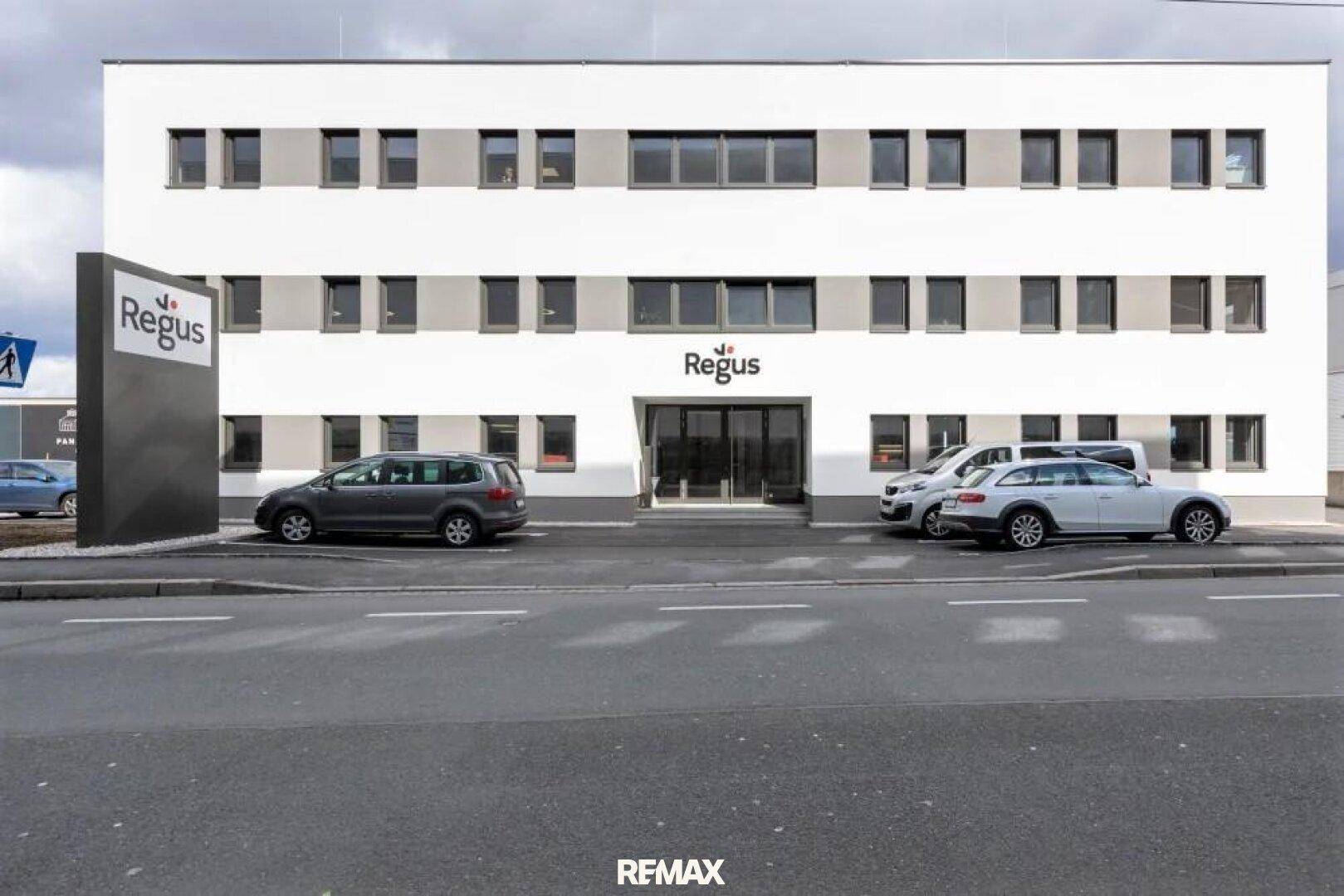 Modernes Bürogebäude mit klarer Architektur, großen Fenstern und Parkplätzen davor für Mitarbeiter und Besucher.
