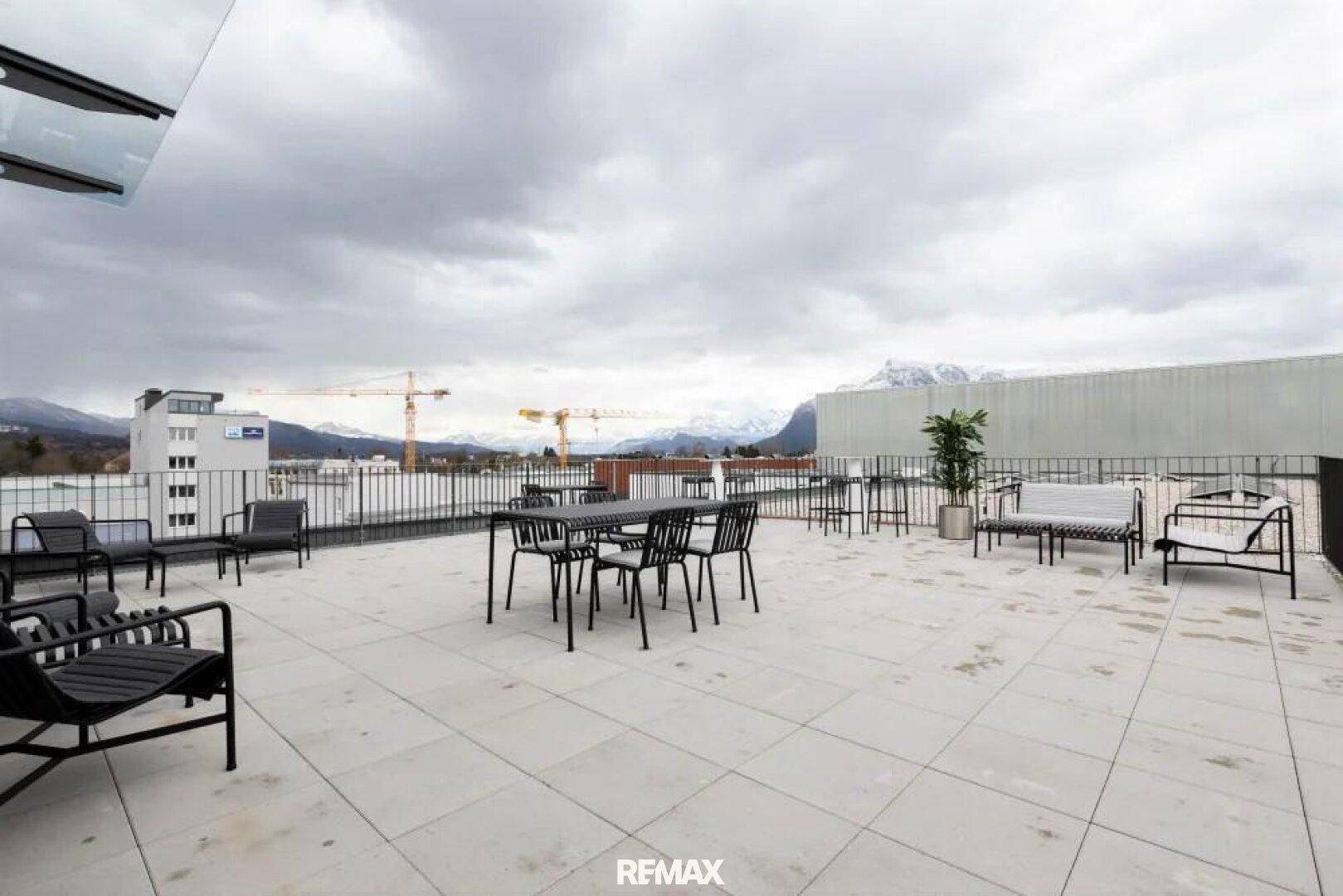 Geräumige Dachterrasse mit modernen Gartenmöbeln und Panoramablick auf die Berge und die Stadt.