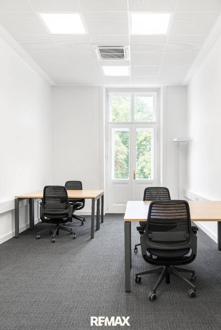 Kleines, helles Büro mit zwei Arbeitsplätzen, Teppichboden und einem großen Fenster mit Blick ins Grüne.