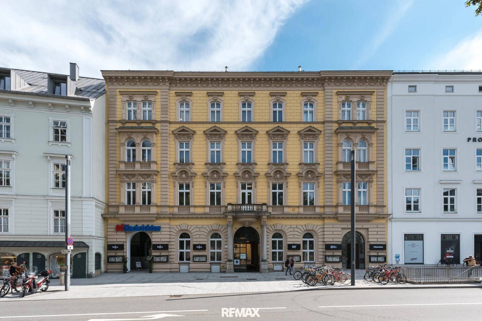 Historische Fassade eines prächtigen Gebäudes mit vielen Fenstern, Balkon und klassischer Architektur.