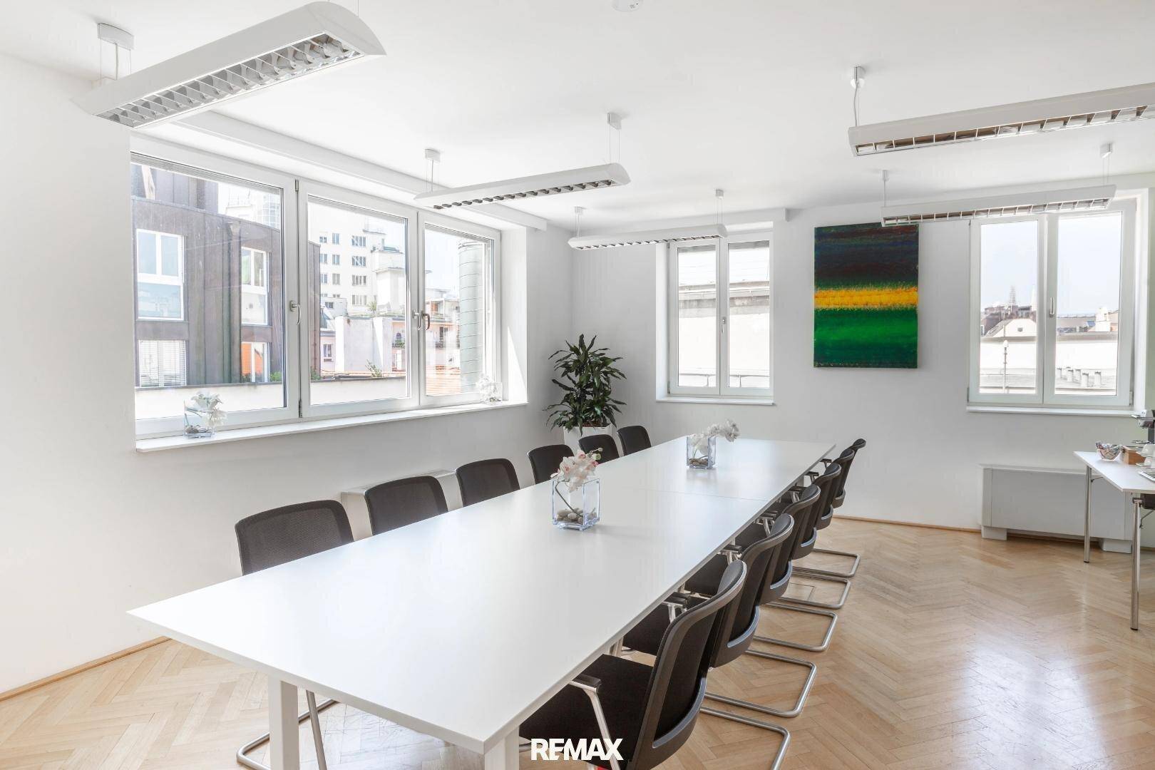 Großer Konferenzraum mit langem Tisch, vielen Stühlen und mehreren Fenstern mit Blick auf die Stadt.