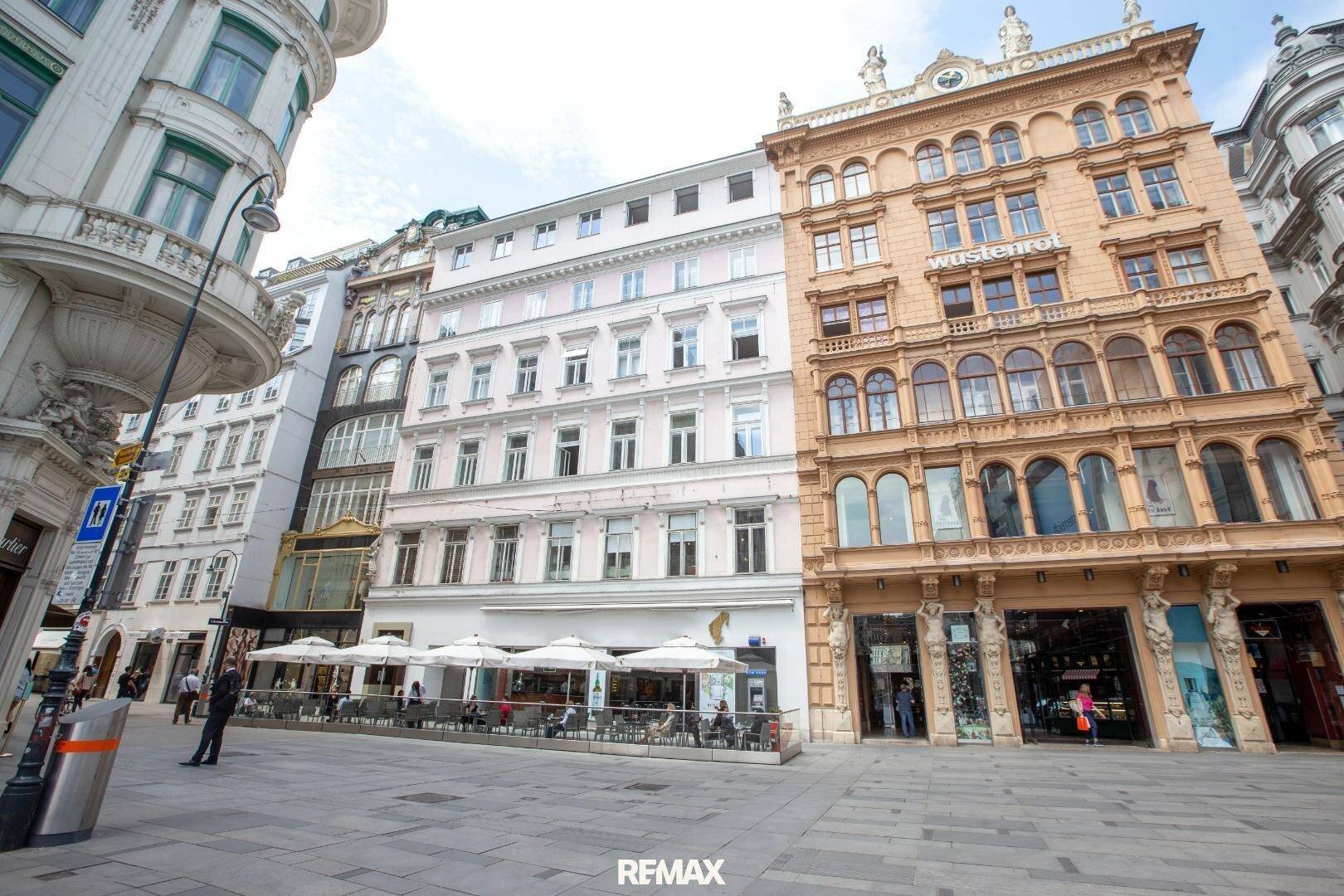 Lebhafte Straße mit historischen Gebäuden, Geschäften und einem Café mit Außenterrasse in der Stadt.