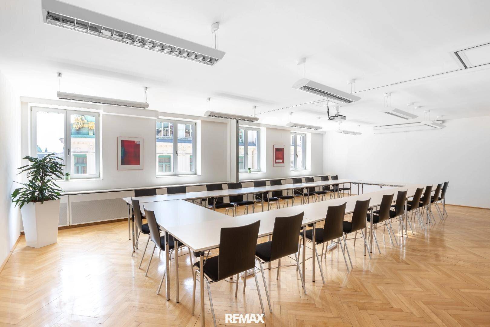 Großer Konferenzraum mit U-förmiger Tischordnung, vielen Fenstern und Parkettboden, ausgestattet mit Beamer.