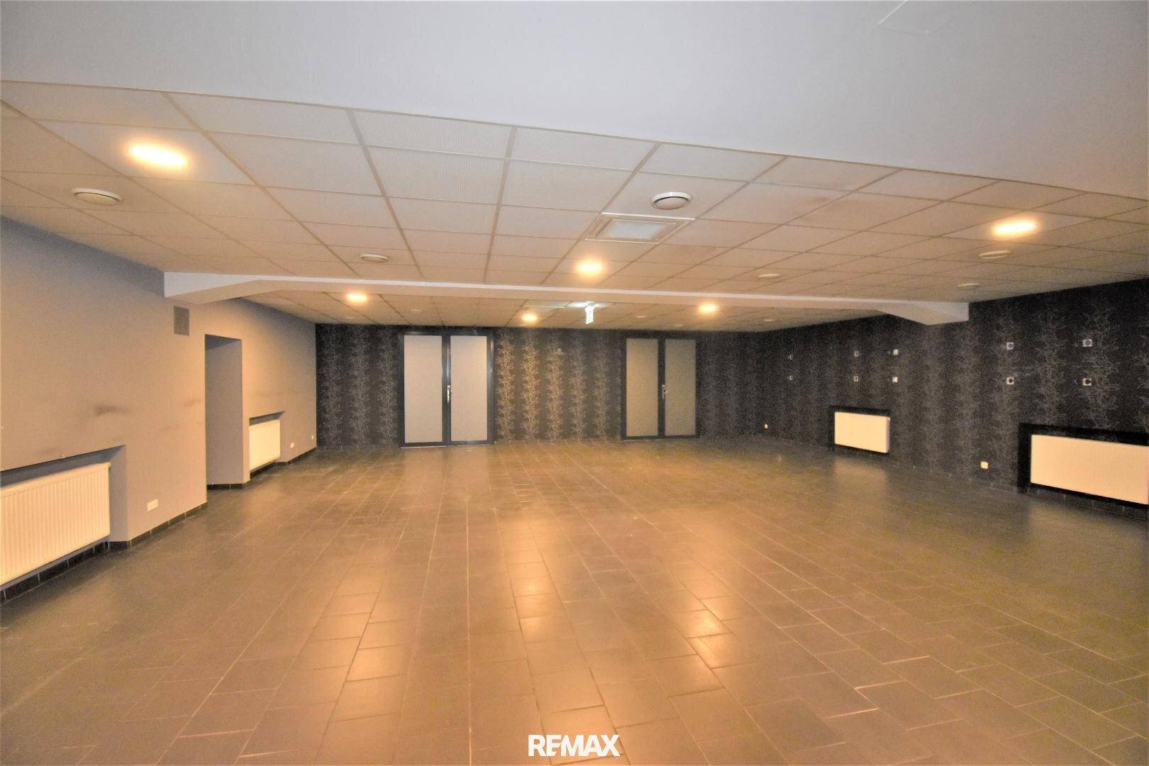 Großer, offener Raum mit Fliesenboden, abgehängter Decke und Heizkörpern, vielseitig nutzbar.